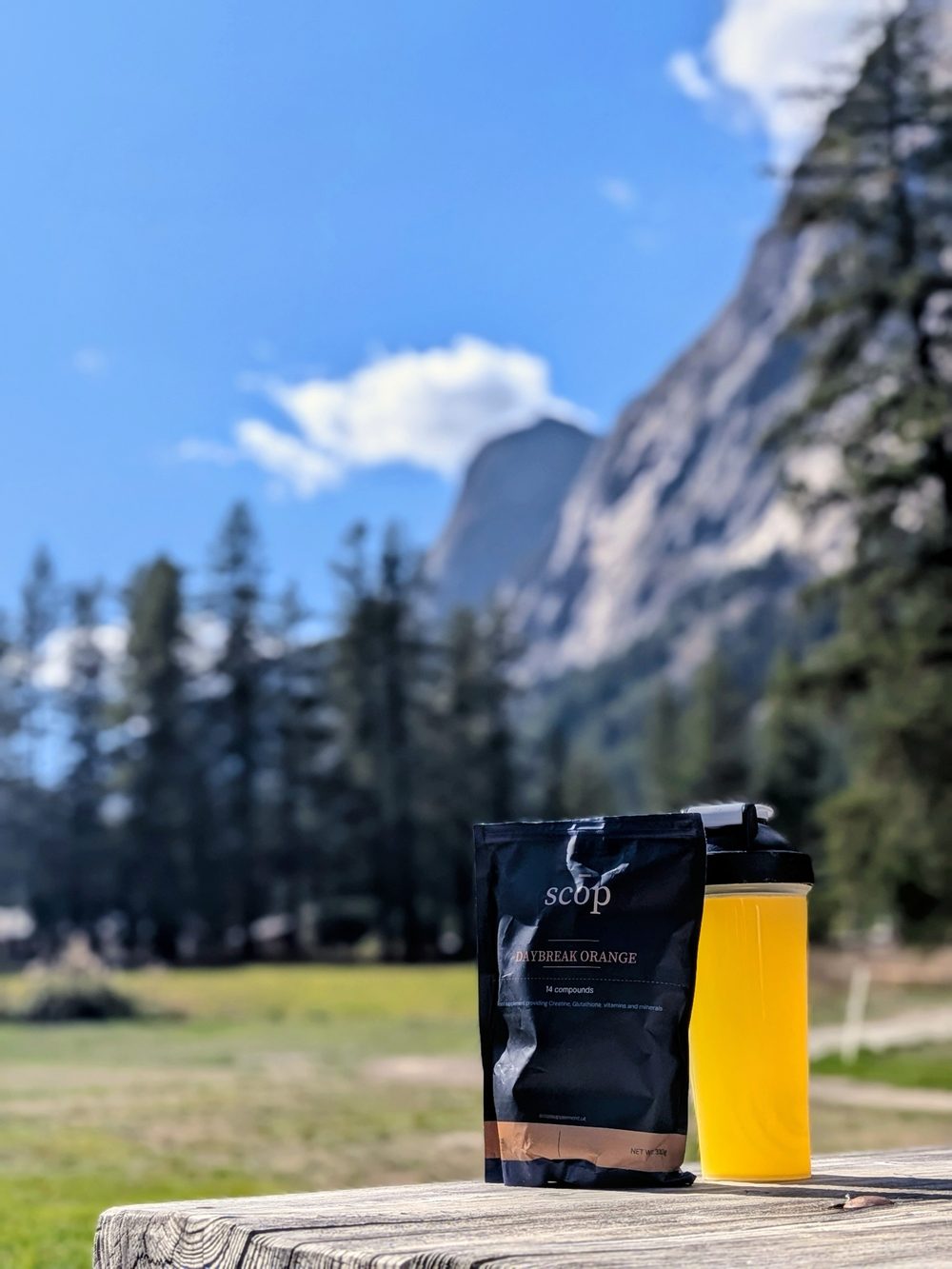 Scōp pouch and a shaker of mixed Daybreak Orange on a picnic table, mountains behind